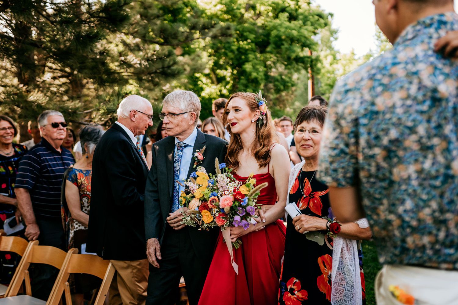 A gathering of wedding guests at an outdoor ceremony with a person in red as the focal point.