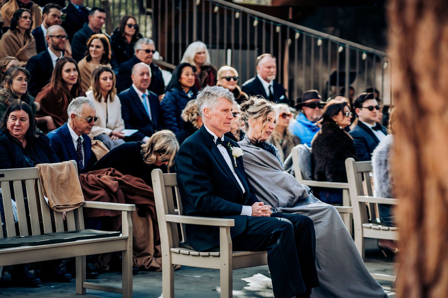 Wedding guests seated on wooden benches during outdoor ceremony.