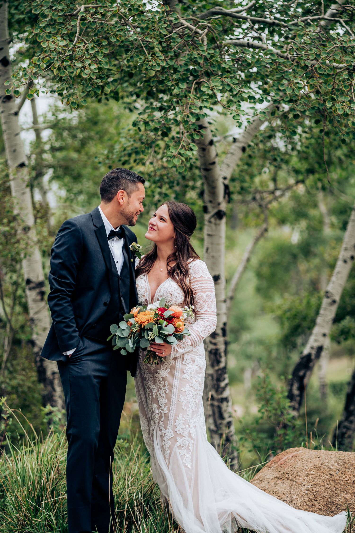 Newlyweds share a tender moment surrounded by aspen trees in a mountain setting.
