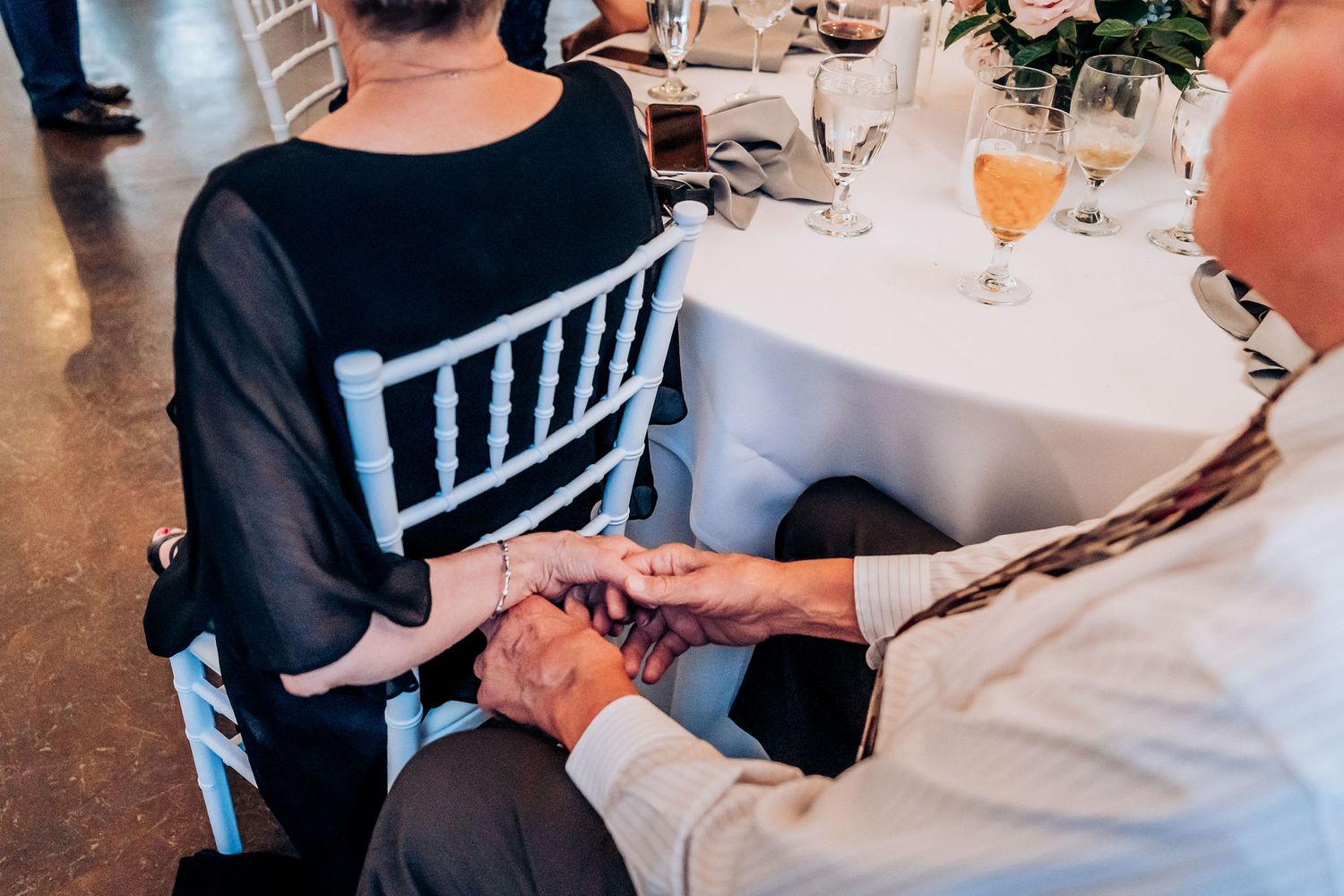 Close-up of hands touching across a wedding reception table with chiavari chairs.