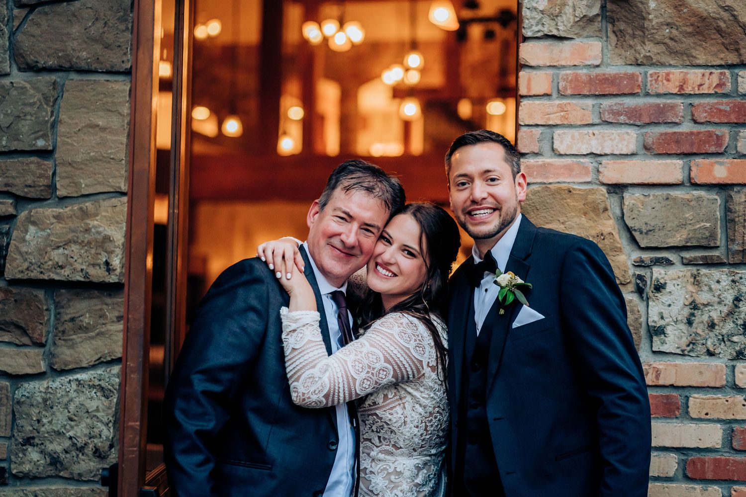 Wedding celebration outside stone building with warm interior lighting visible through doorway.
