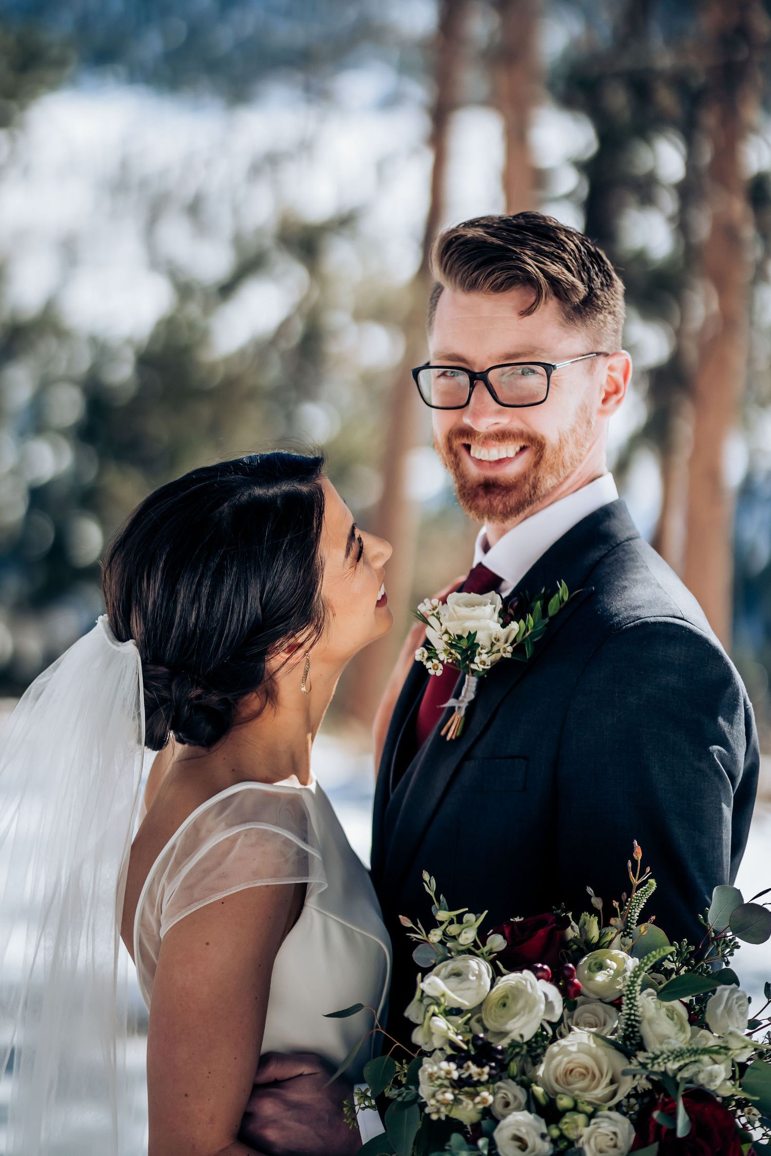 A tender moment between newlyweds with a stunning winter forest backdrop.