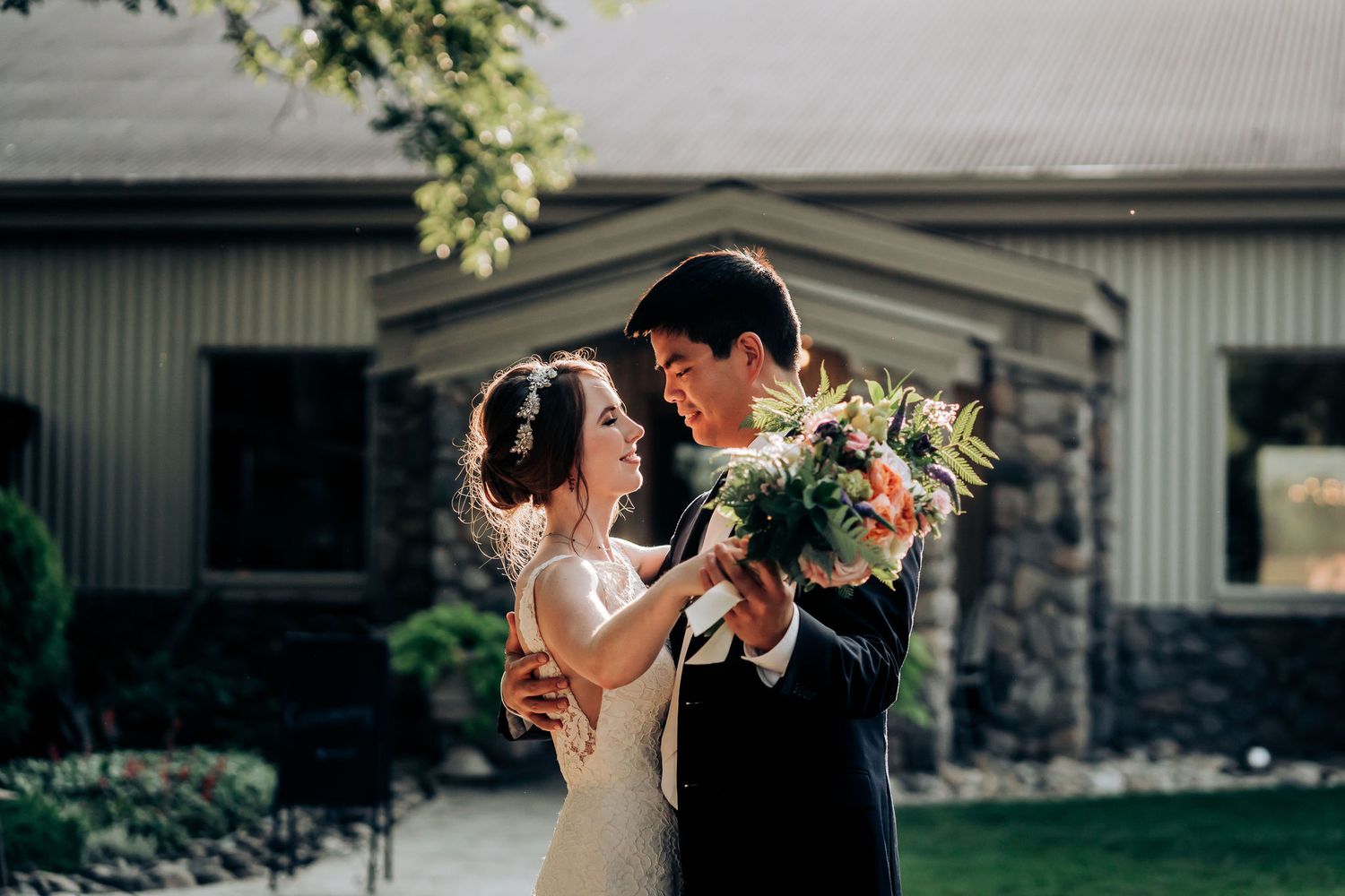 Joyful wedding couple dancing with floral bouquet in outdoor garden setting.