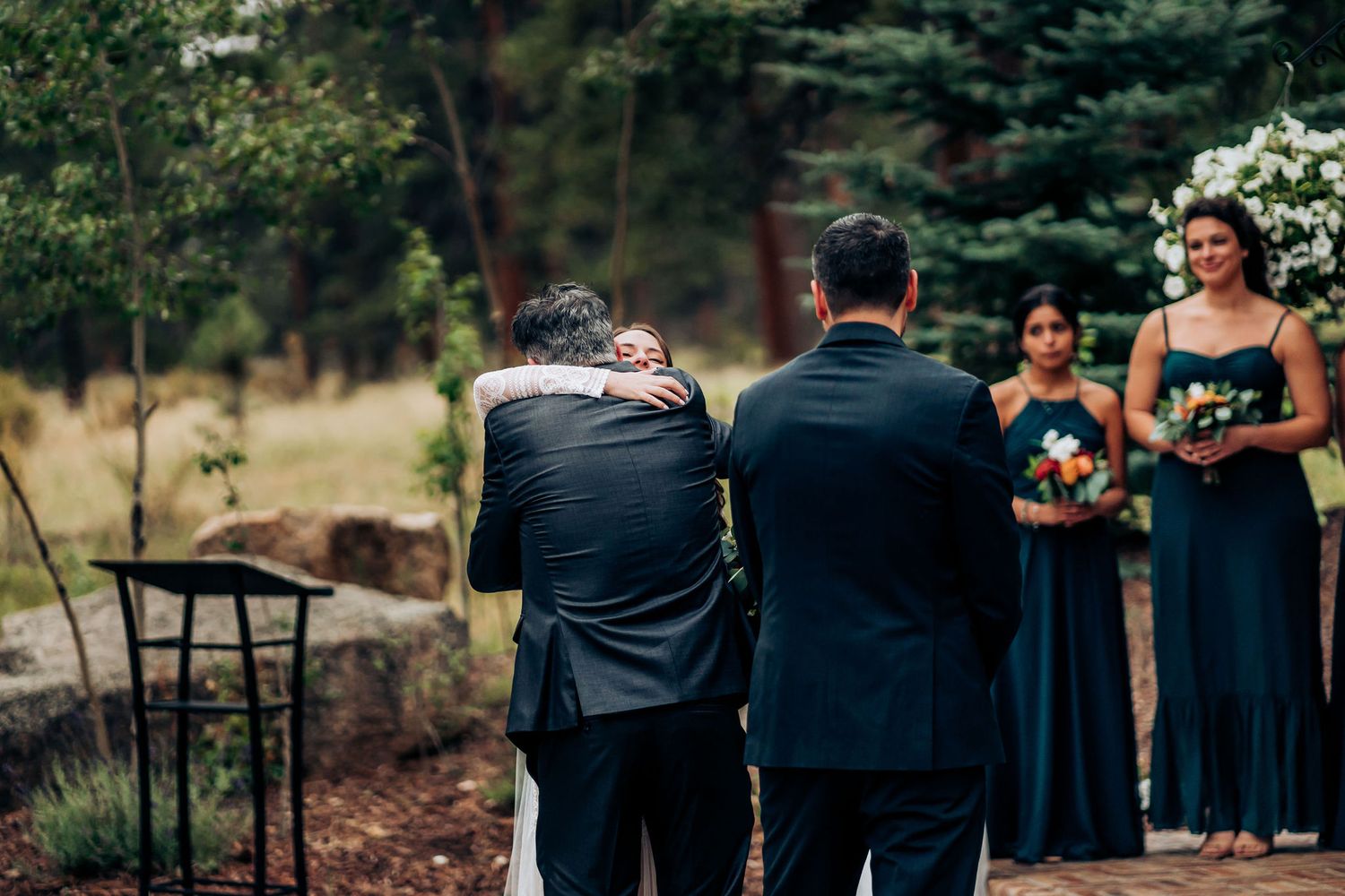 Emotional embrace during outdoor wedding ceremony with attendants in navy blue dresses.