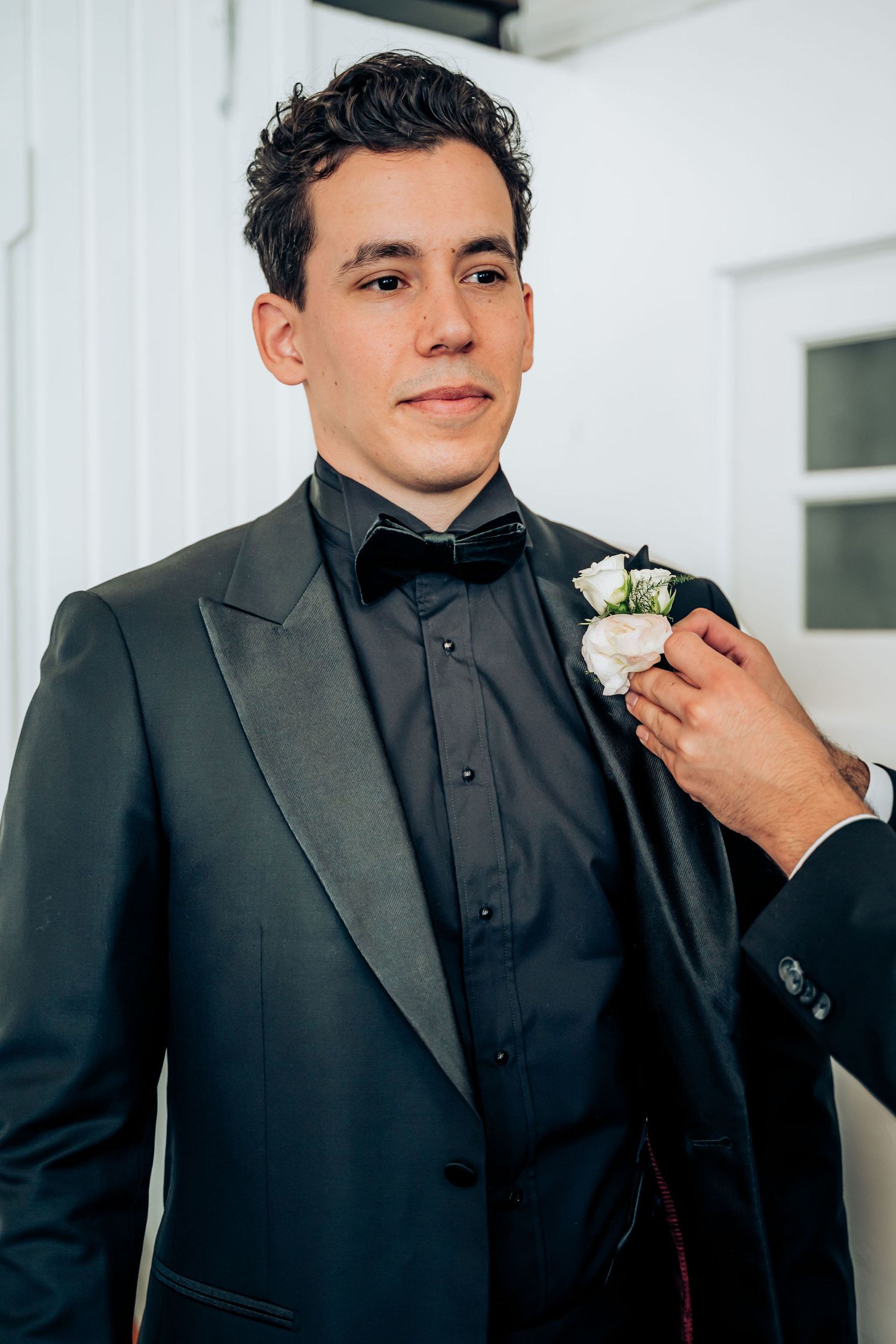 Groom in black tuxedo with bow tie and white boutonniere getting ready for wedding.