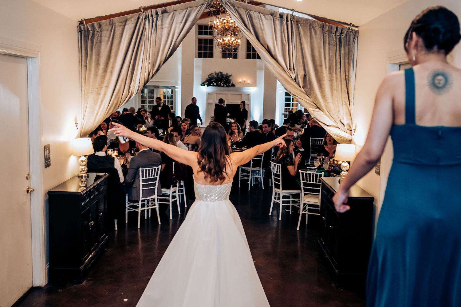Bride celebrates with outstretched arms in reception venue with elegant draping.