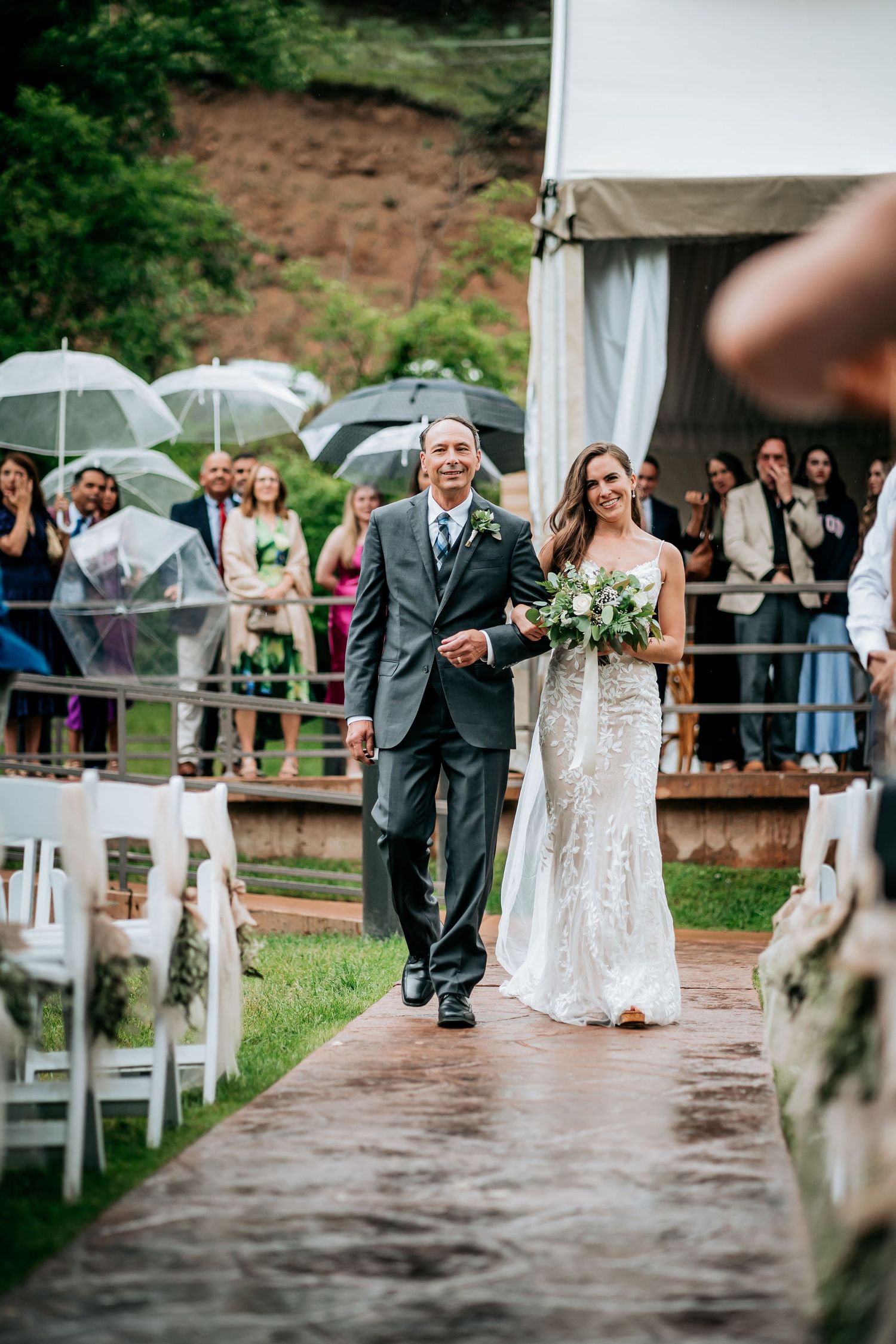 Wedding ceremony procession on a rainy day with guests holding clear umbrellas.