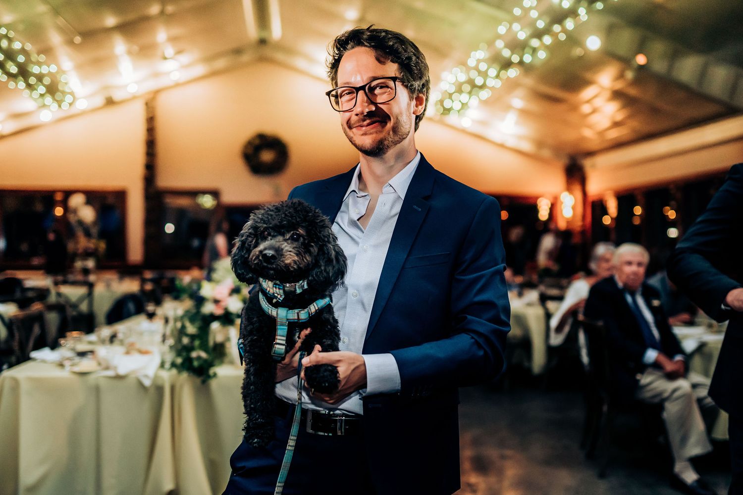 A guest holds a small black pug dog during an elegant indoor wedding reception.