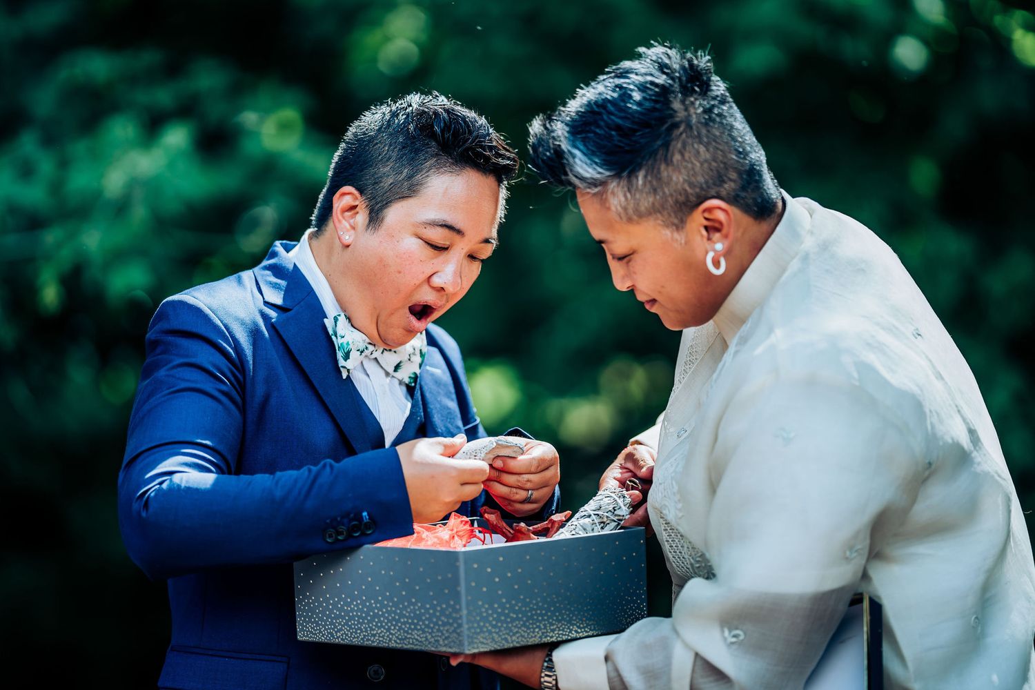 Two people share a joyful moment while looking at items in a box during an outdoor celebration.