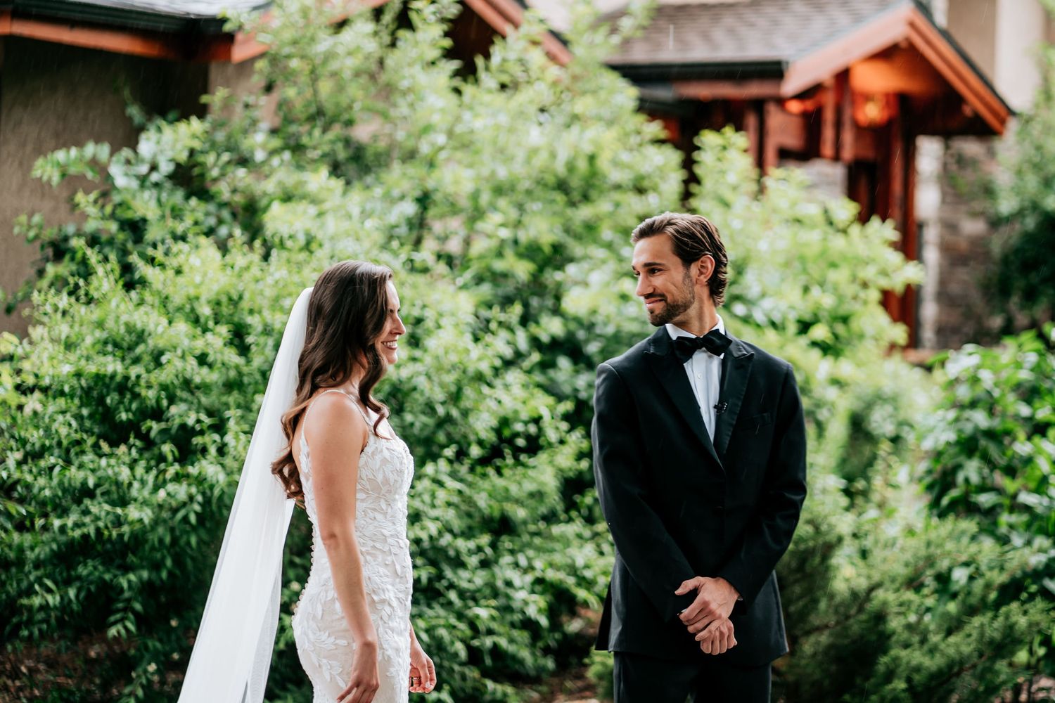 A couple shares a romantic moment in their wedding attire against a backdrop of green foliage.