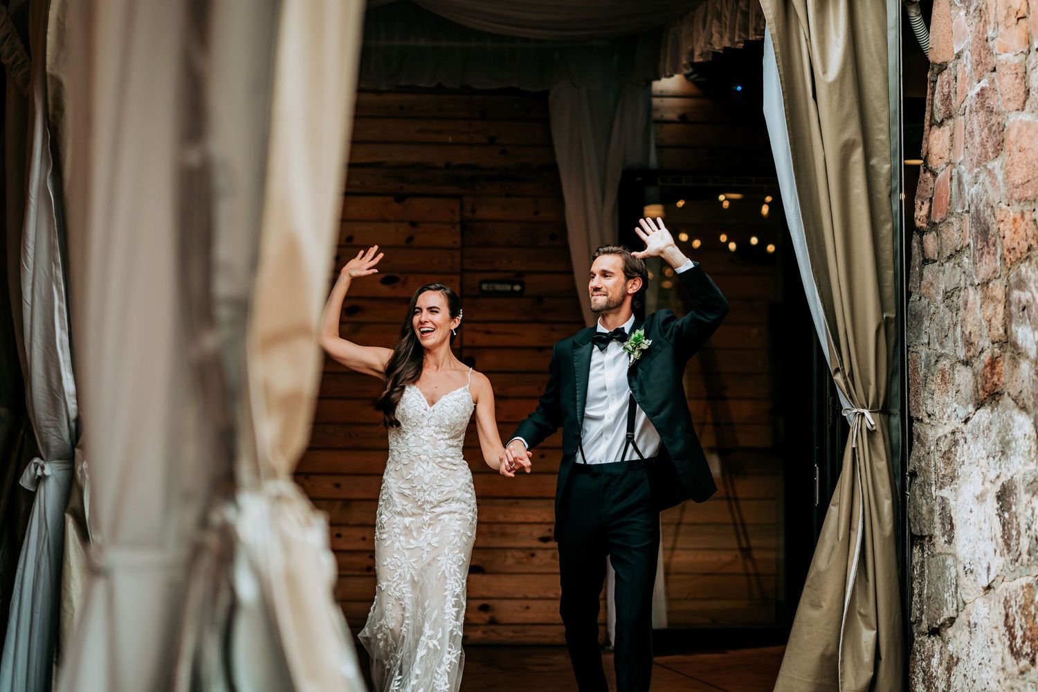 A newlywed couple makes their grand entrance through draped curtains at their wedding reception.
