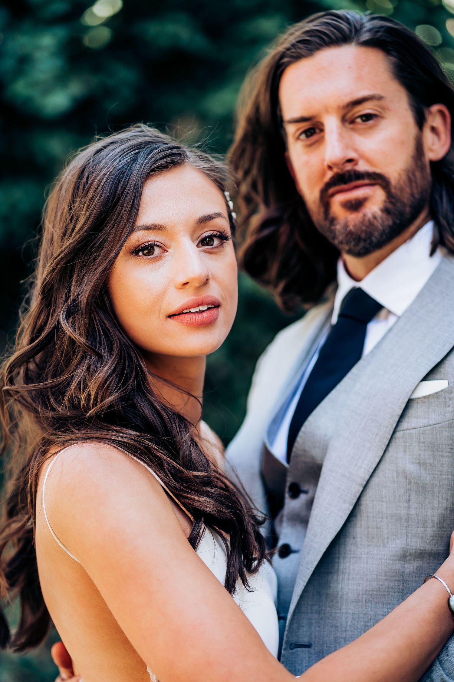Elegant wedding portrait featuring a couple in formal attire against a blurred natural background.