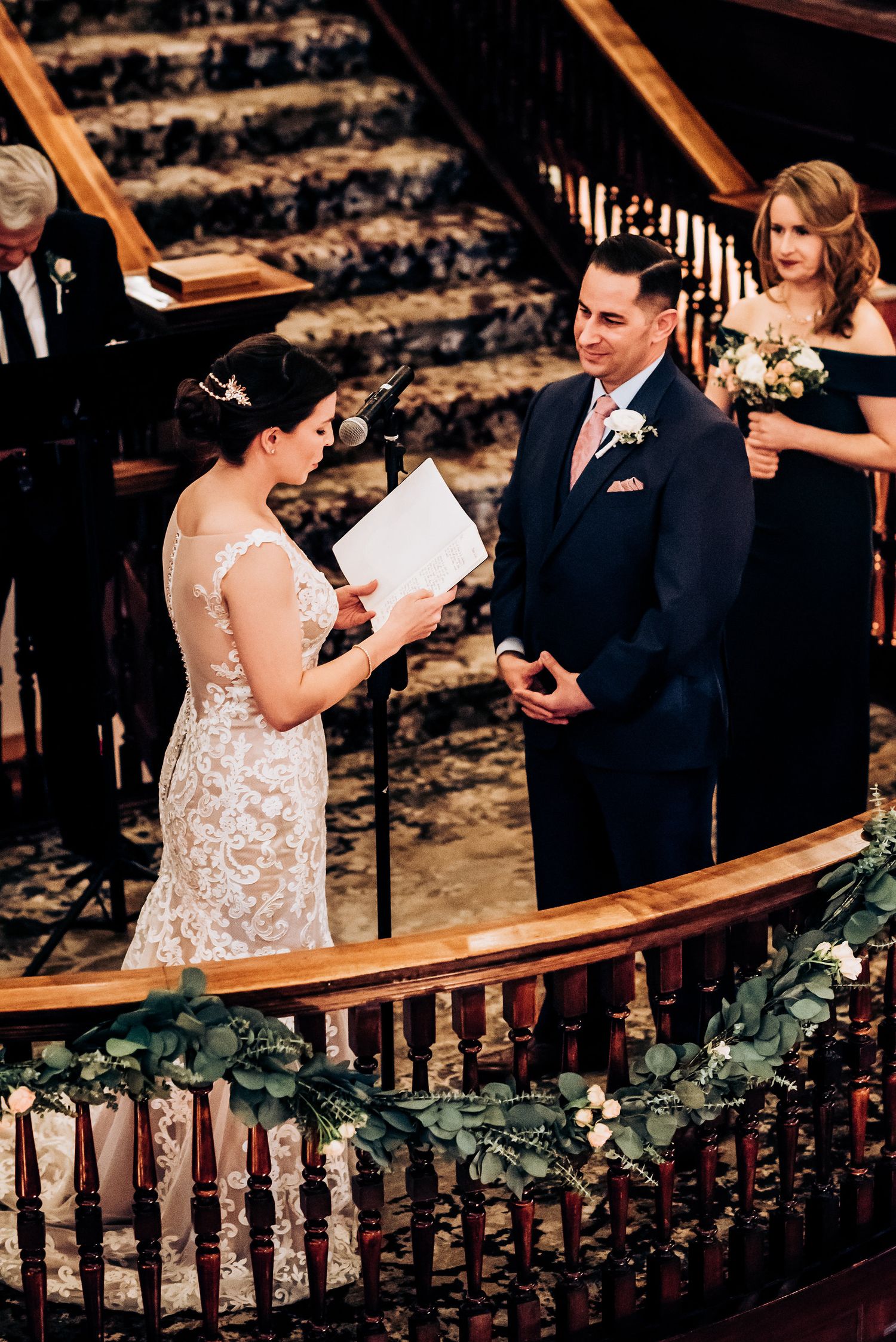 Wedding ceremony with elegant floral garland decorating the wooden railing in a historic venue.