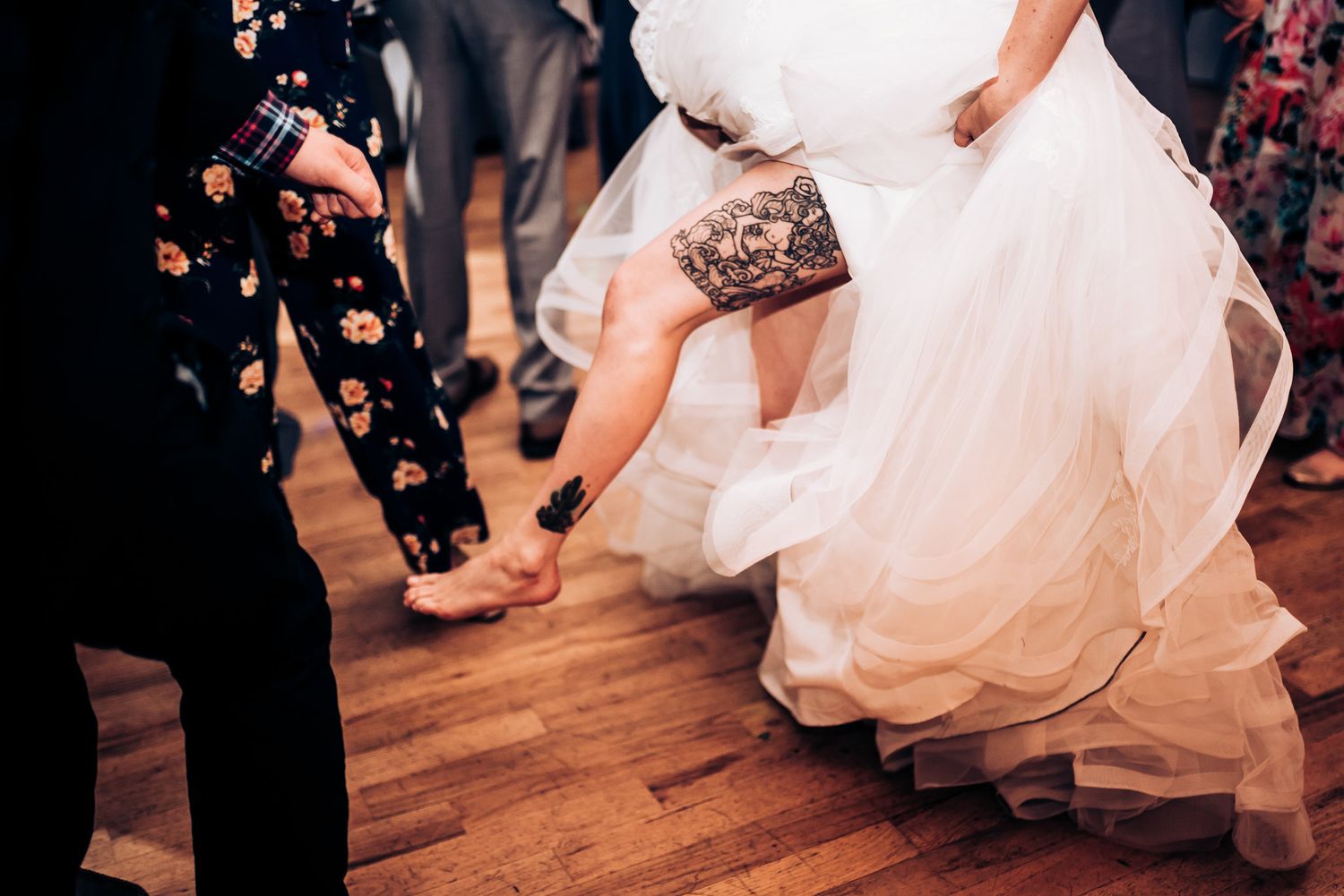 Close-up of wedding dress details as dancers move on wooden dance floor.