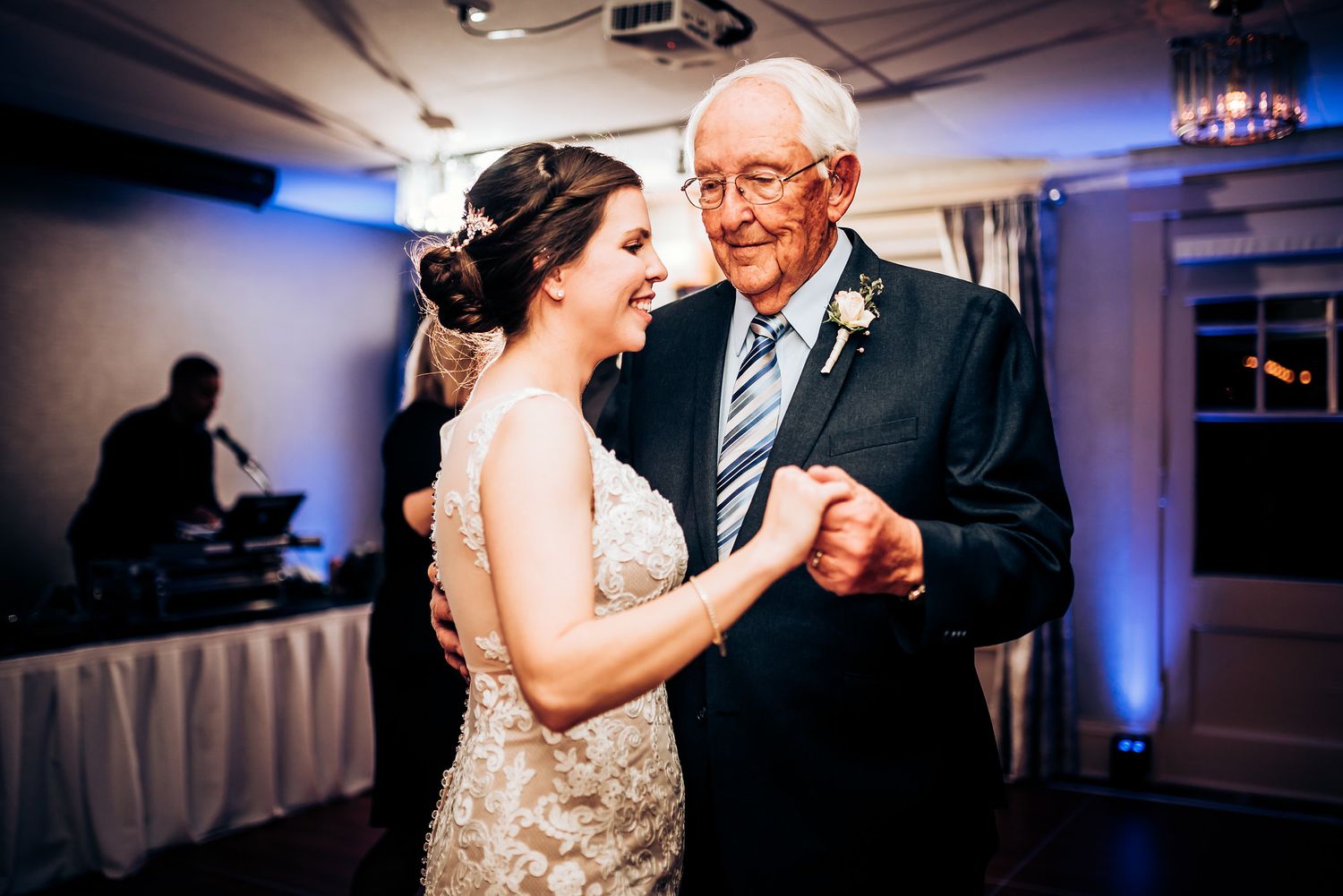 A tender dance moment between a bride in lace and an elderly guest at a wedding reception.