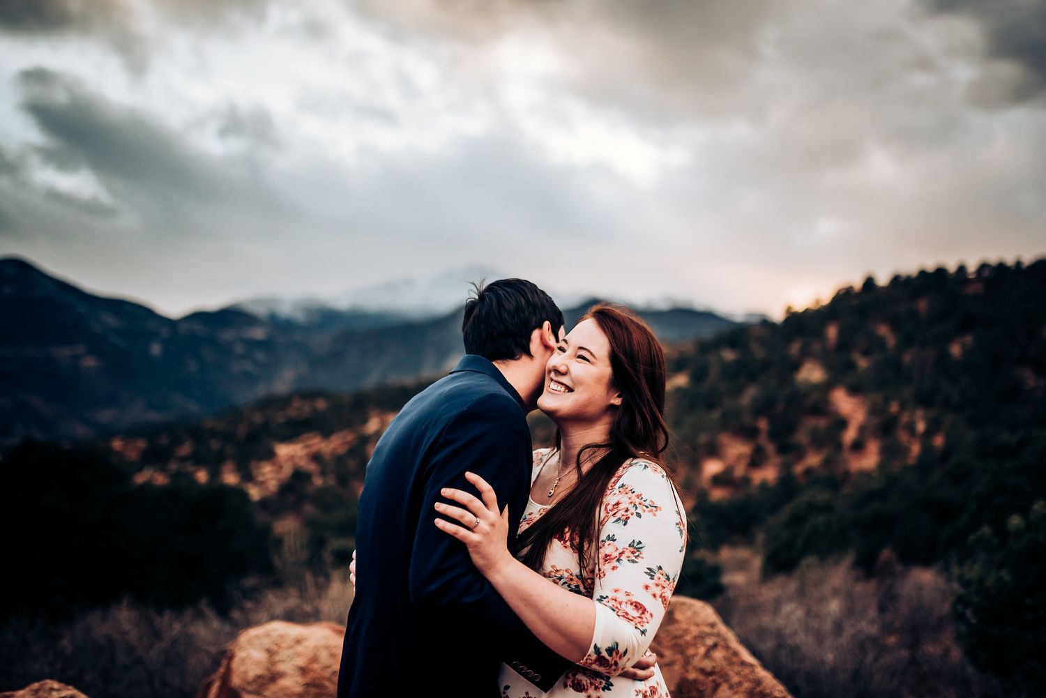 A tender romantic moment captured against dramatic mountain scenery at dusk.