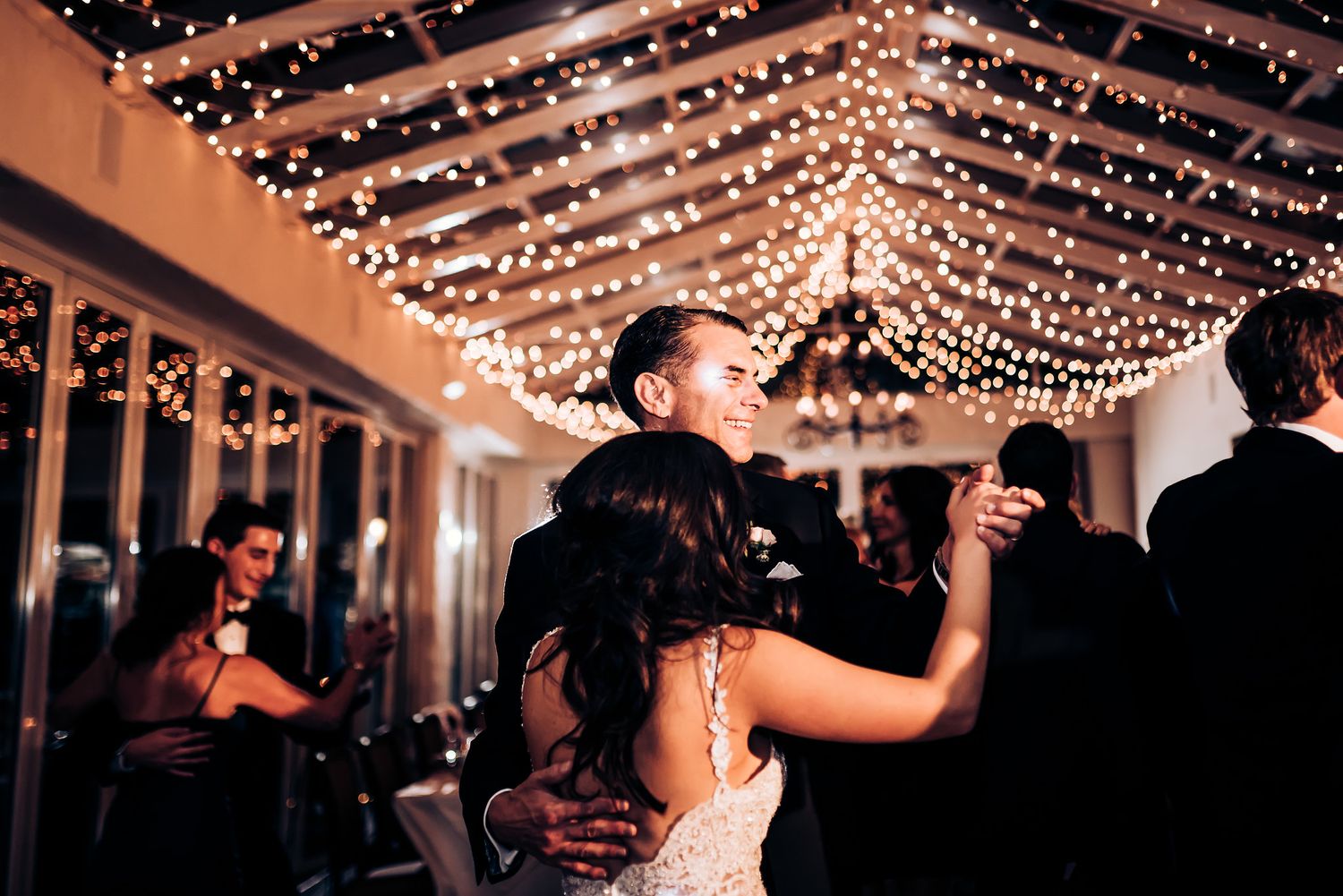Couples dancing beneath canopy of string lights at elegant wedding reception.
