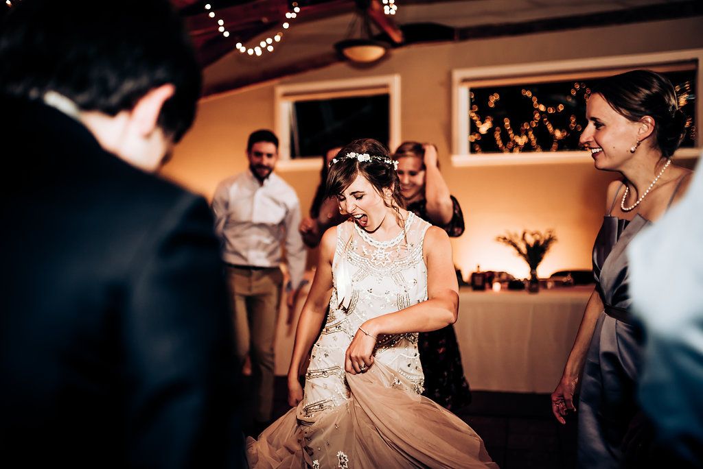 Wedding guests celebrate with dancing and laughter at a warmly lit indoor reception.
