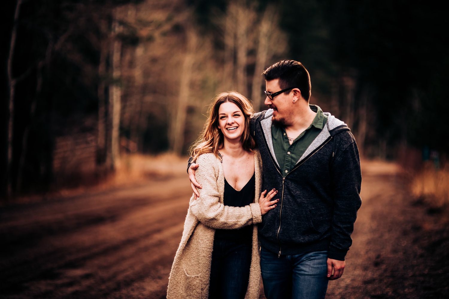 Couple laughing together on dirt path during autumn photo session.