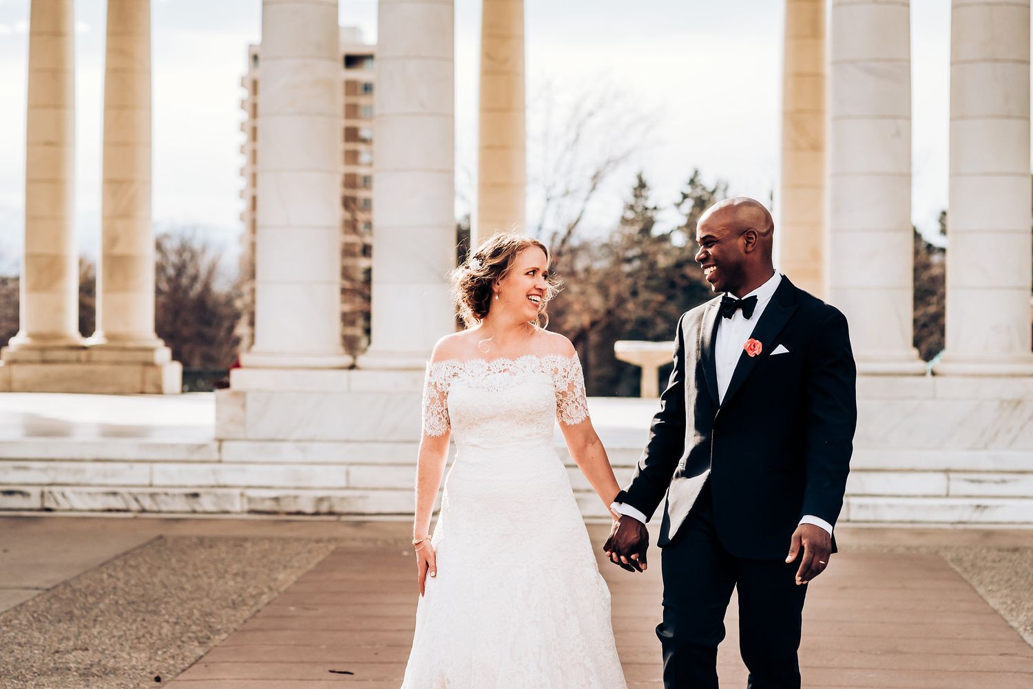 Happy couple shares a joyful moment walking between grand white columns.