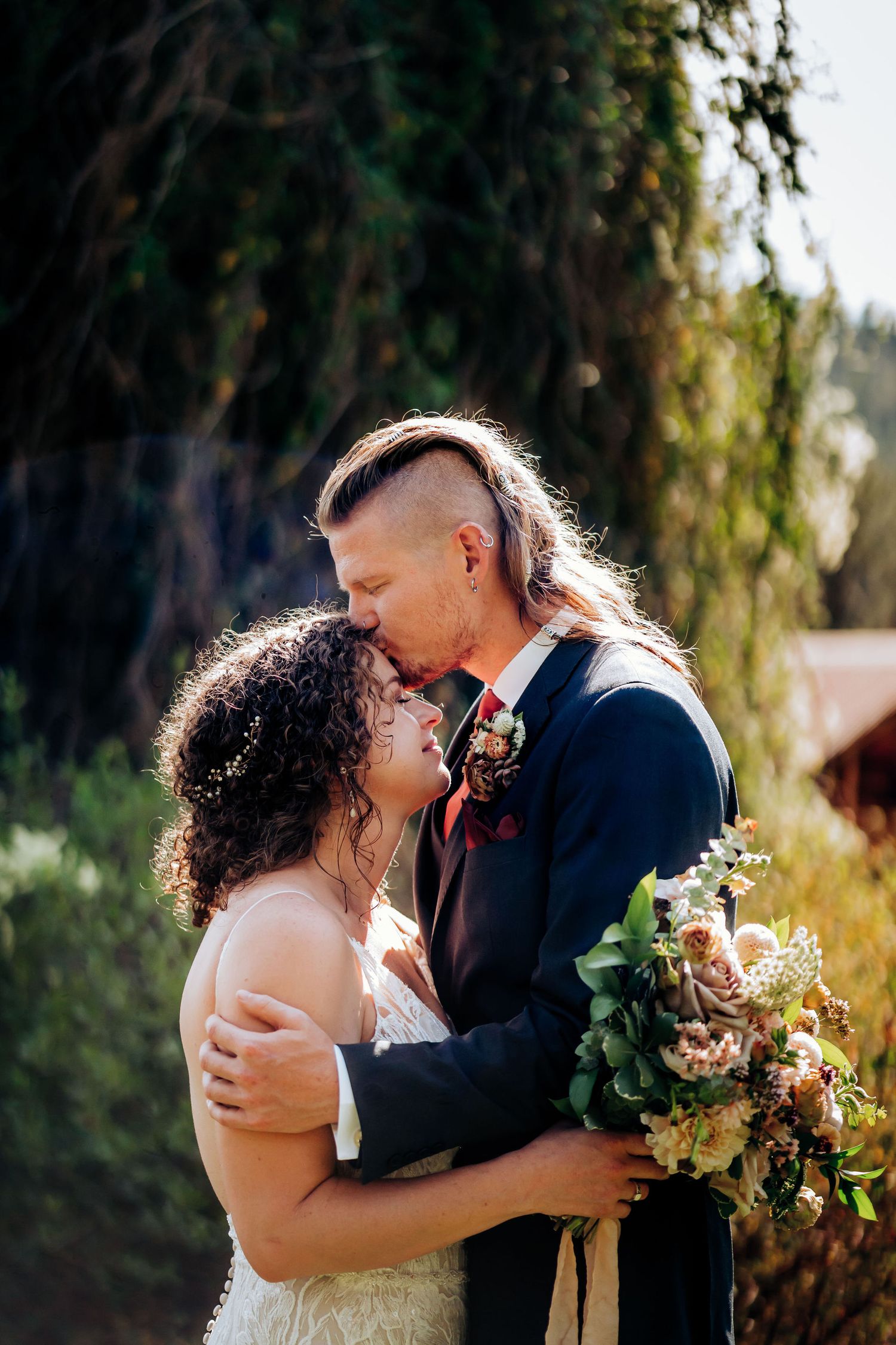 An intimate wedding portrait showing a couple in a tender embrace with a rustic backdrop.