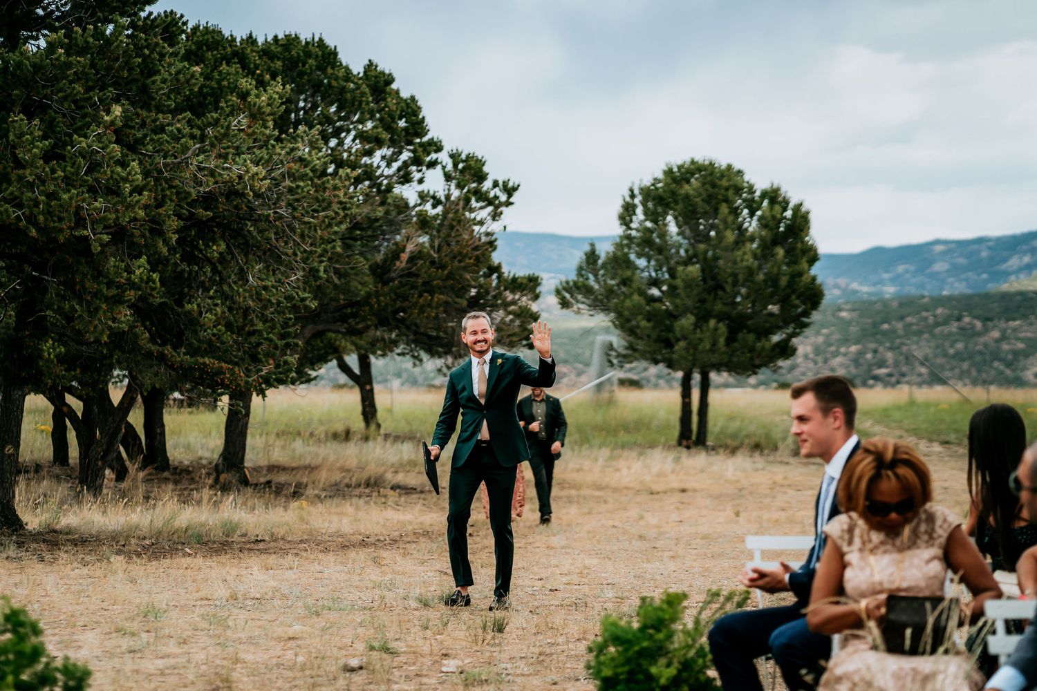 Wedding ceremony moment with guests seated in rustic outdoor mountain setting.