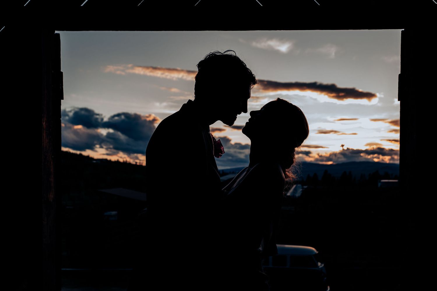 Silhouetted couple embracing against dramatic sunset sky with dark clouds.