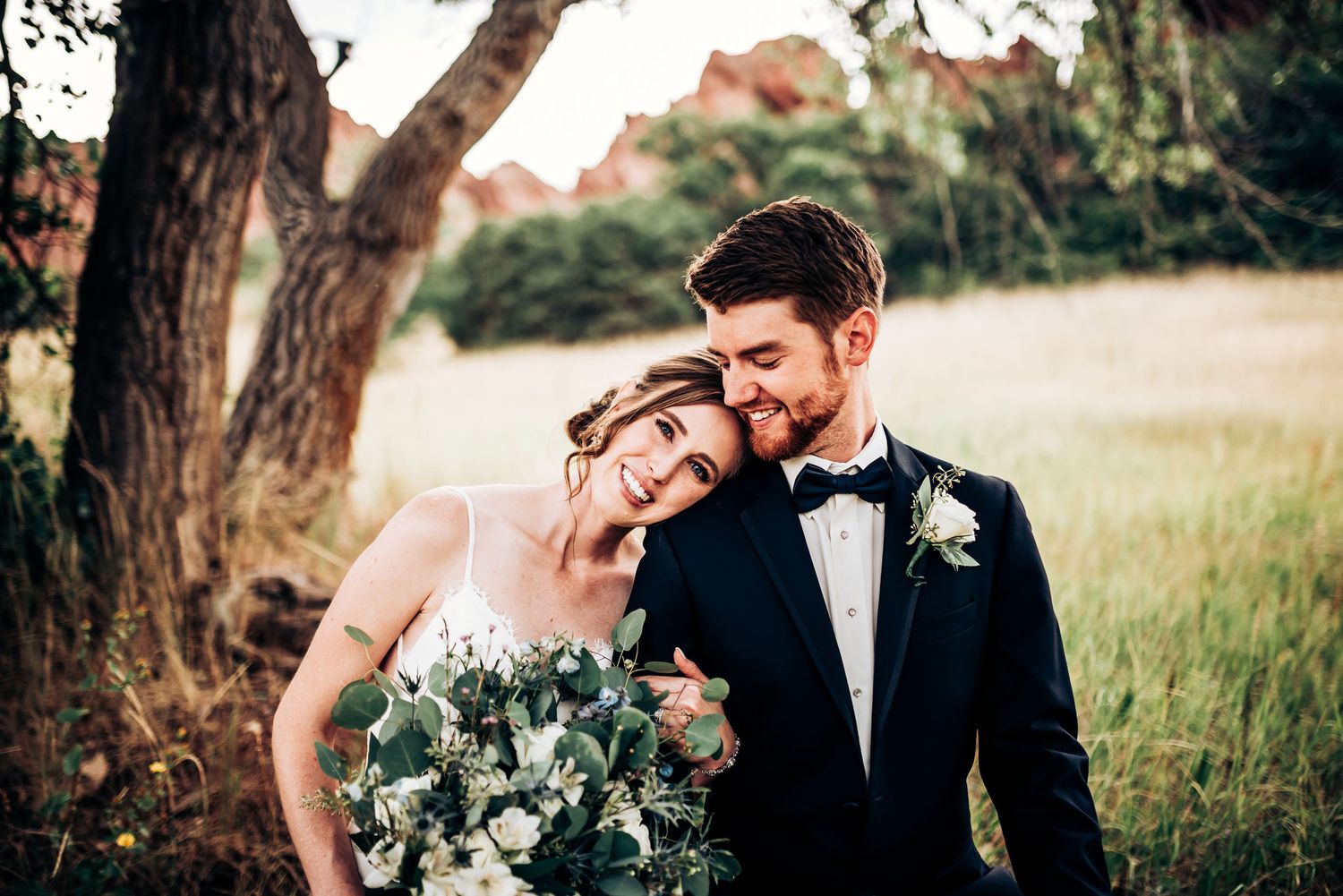 Joyful couple shares tender moment under tree with sunlit field in background.