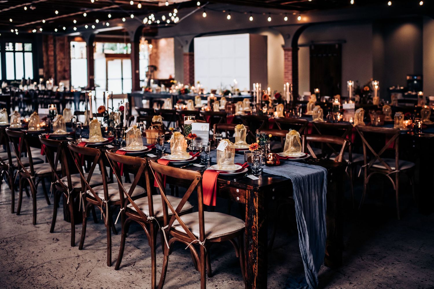 Industrial wedding venue with cross-back chairs and string lights creating romantic atmosphere.