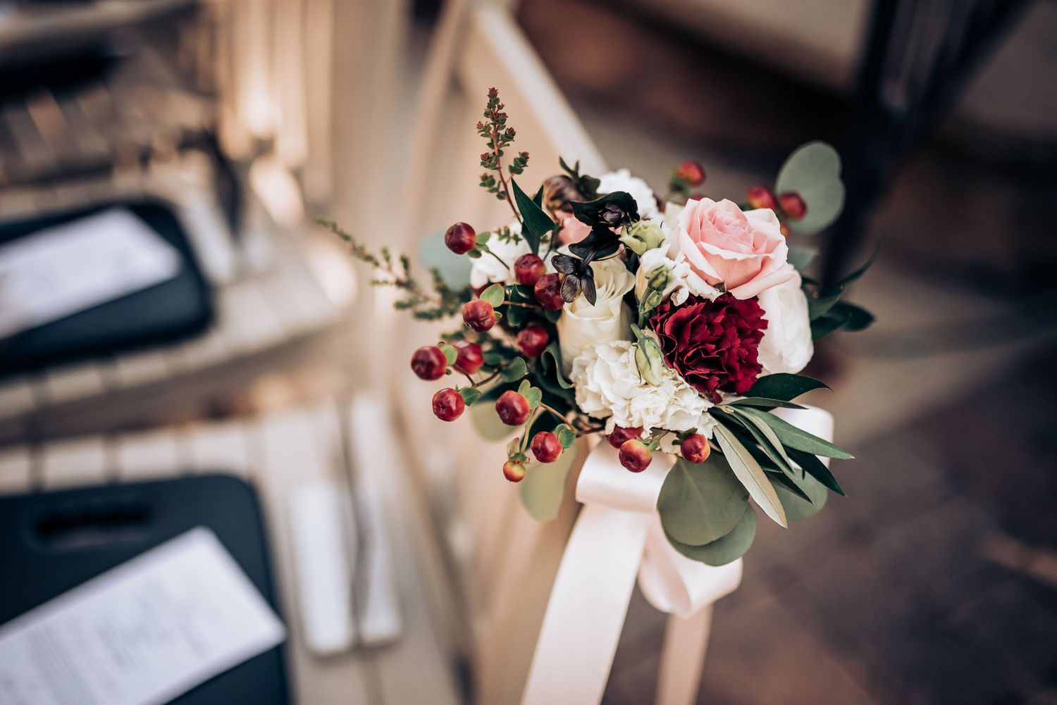 A romantic wedding bouquet with pink roses, burgundy flowers, and eucalyptus tied with white ribbon.