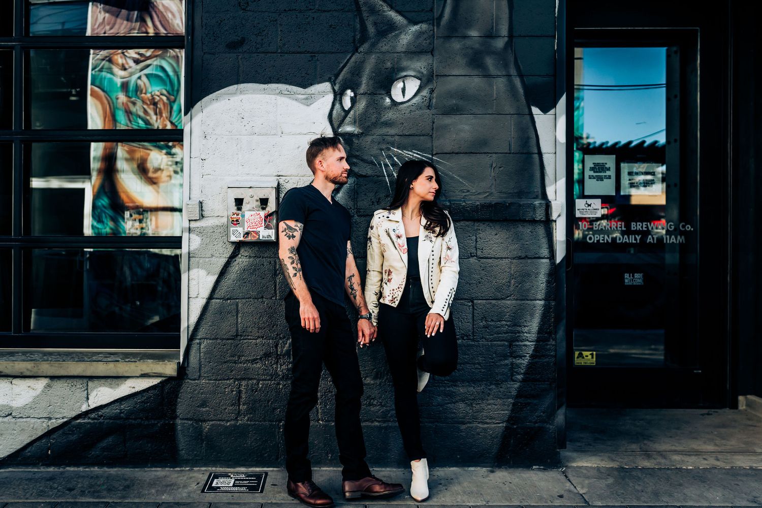 Couple poses in front of large black and white cat street art mural.