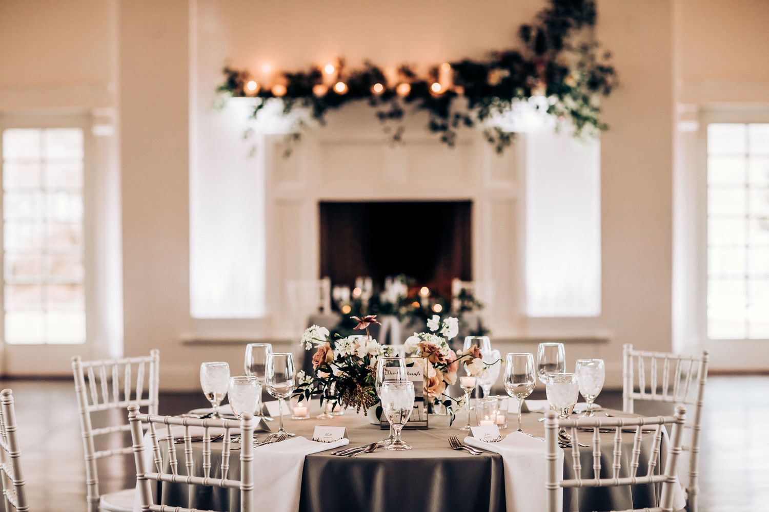 Wedding reception tables with silver chiavari chairs arranged around a central fireplace.