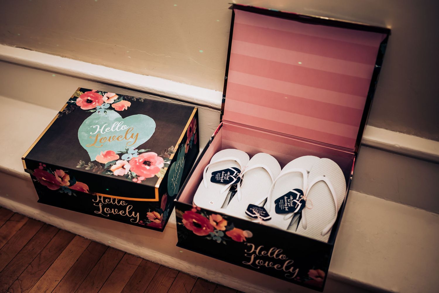 Two decorative floral boxes with wedding slippers displayed on hardwood flooring.