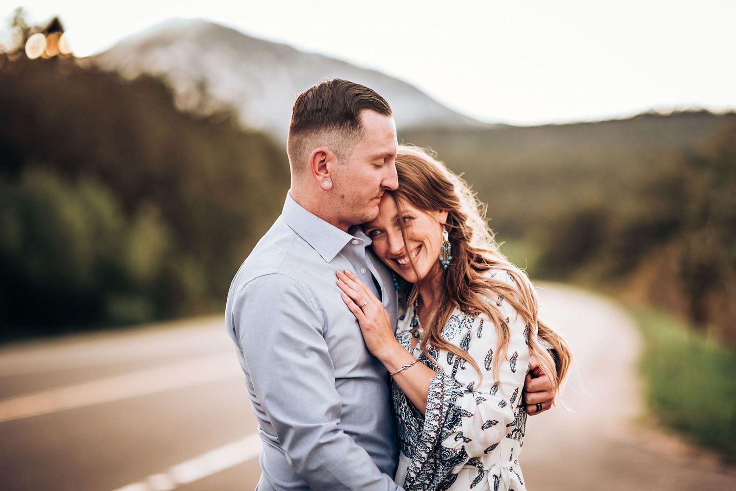 A couple shares an emotional moment during their mountain road photoshoot at sunset.