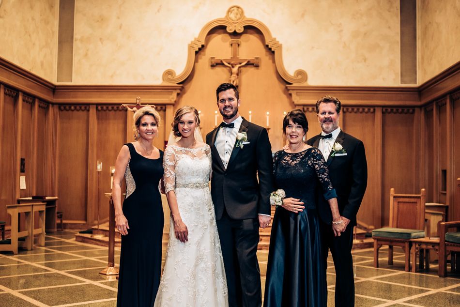 Formal wedding party portrait in a traditional church sanctuary with wooden paneling.
