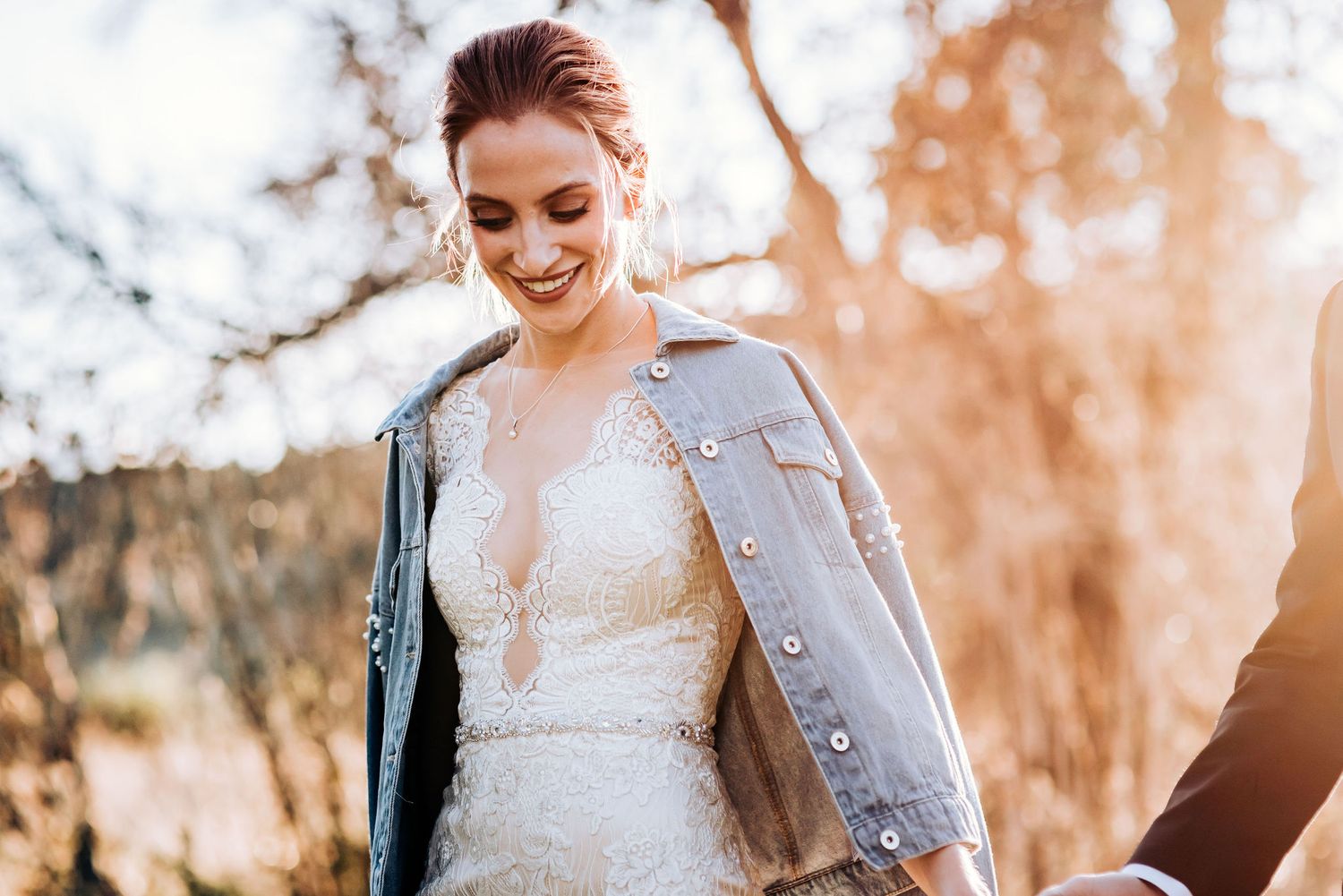Joyful bride wearing lace dress and denim jacket in warm sunset lighting.