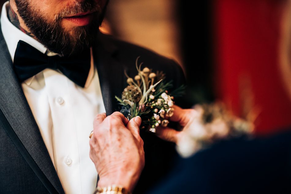 Close-up of boutonniere being adjusted on a formal black tuxedo with bow tie.