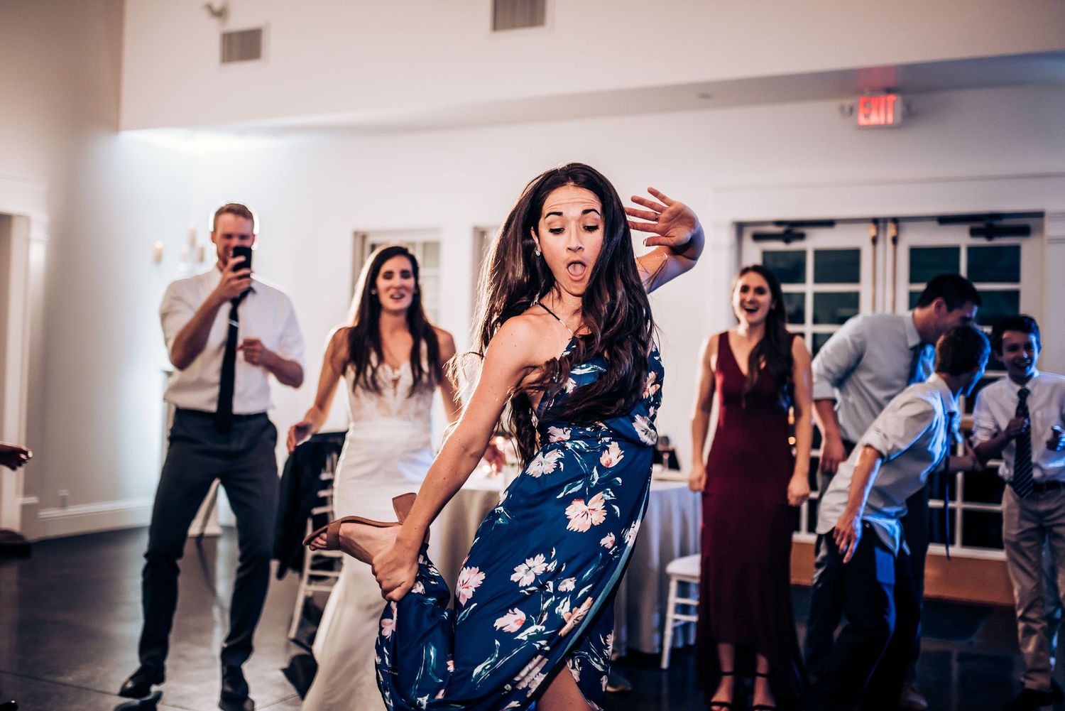 Party guests dance enthusiastically at a wedding reception in a brightly lit indoor venue.