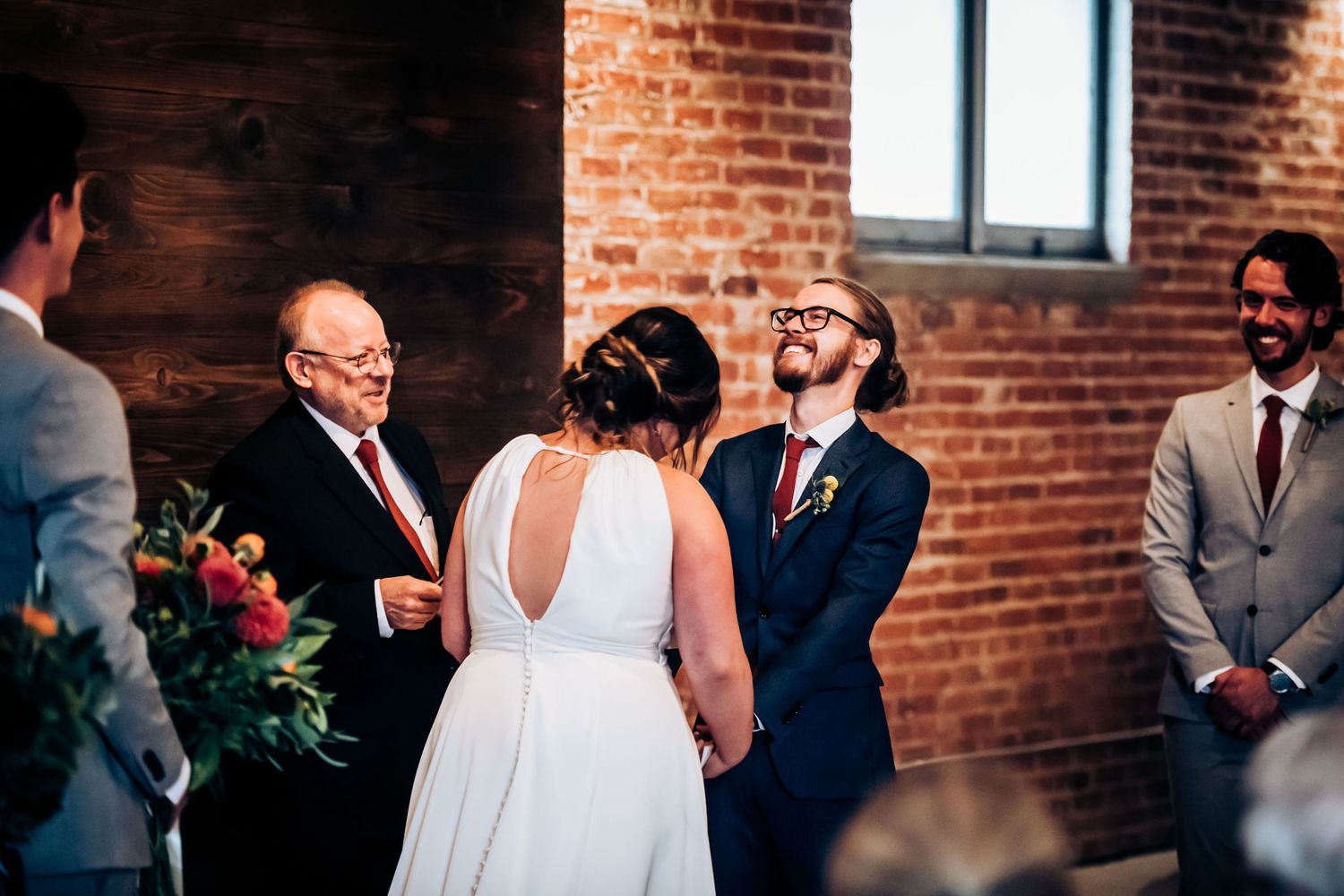 Wedding ceremony in progress inside a rustic brick-walled venue with natural lighting.