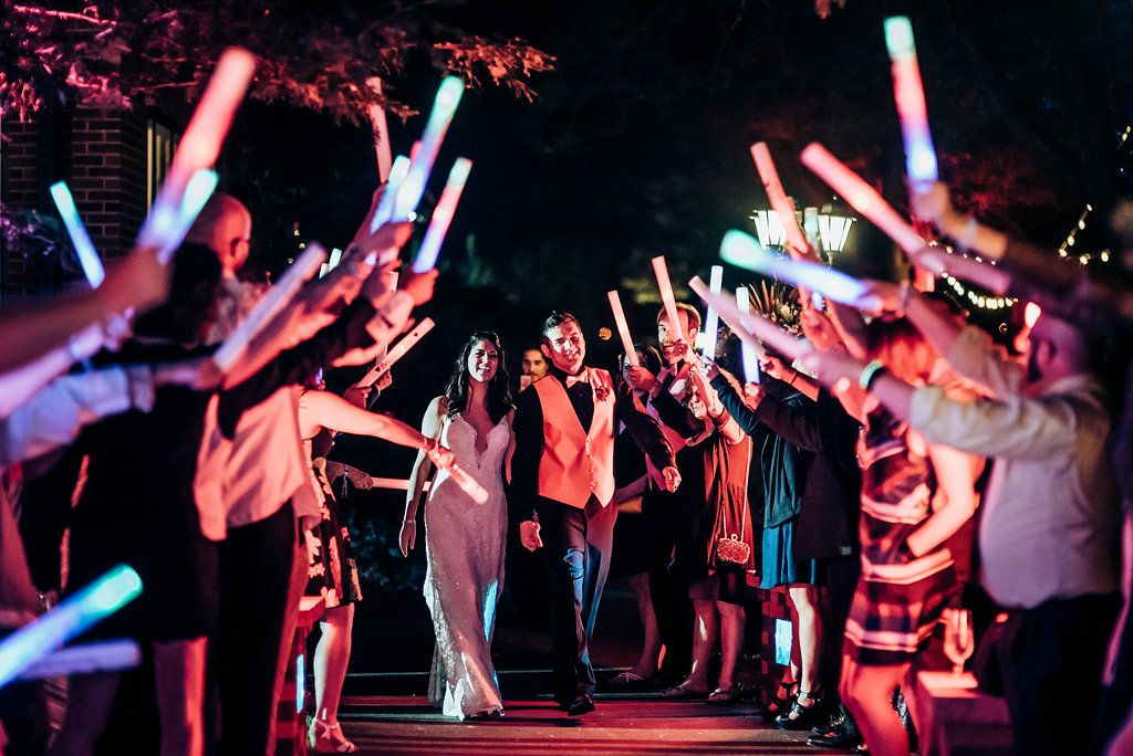 Wedding guests creating a tunnel of colorful LED light wands during evening celebrations.
