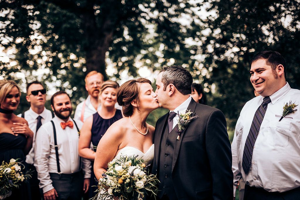 Joyful wedding moment captured outdoors with wedding party looking on.