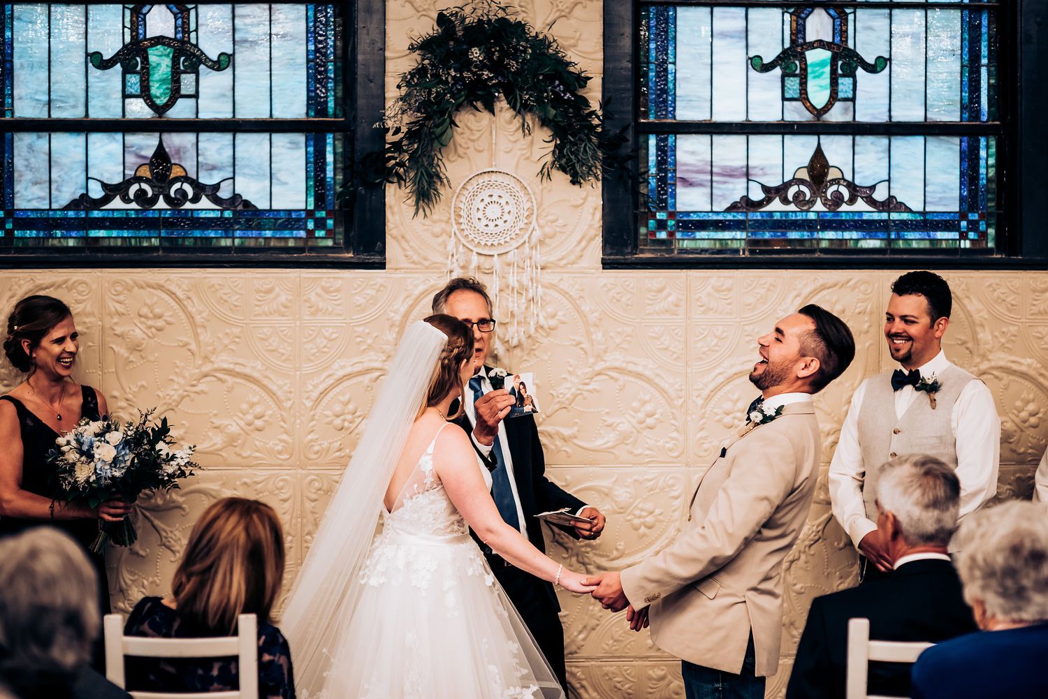 Wedding ceremony in front of stained glass windows with decorative wall details.