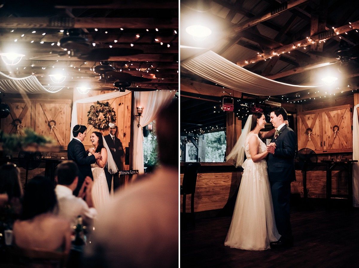 A couple shares their first dance at a rustic barn wedding reception with twinkling lights overhead.