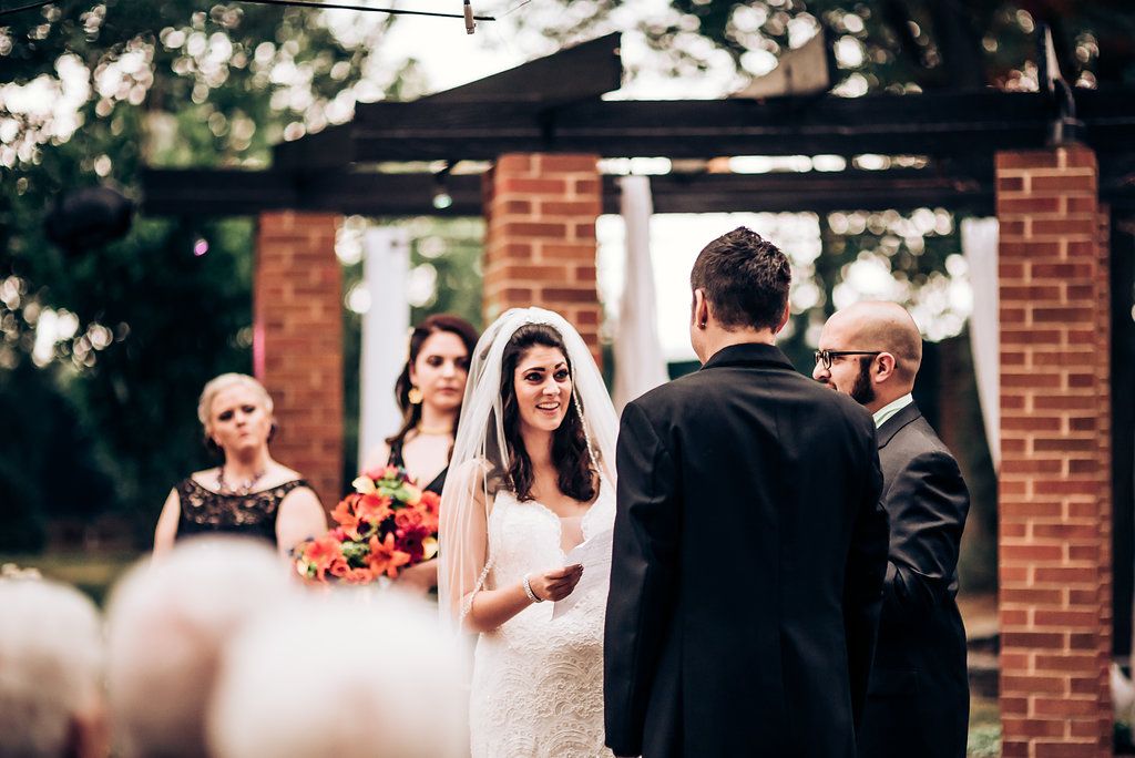 Wedding ceremony in progress at outdoor brick venue with vibrant floral decorations.
