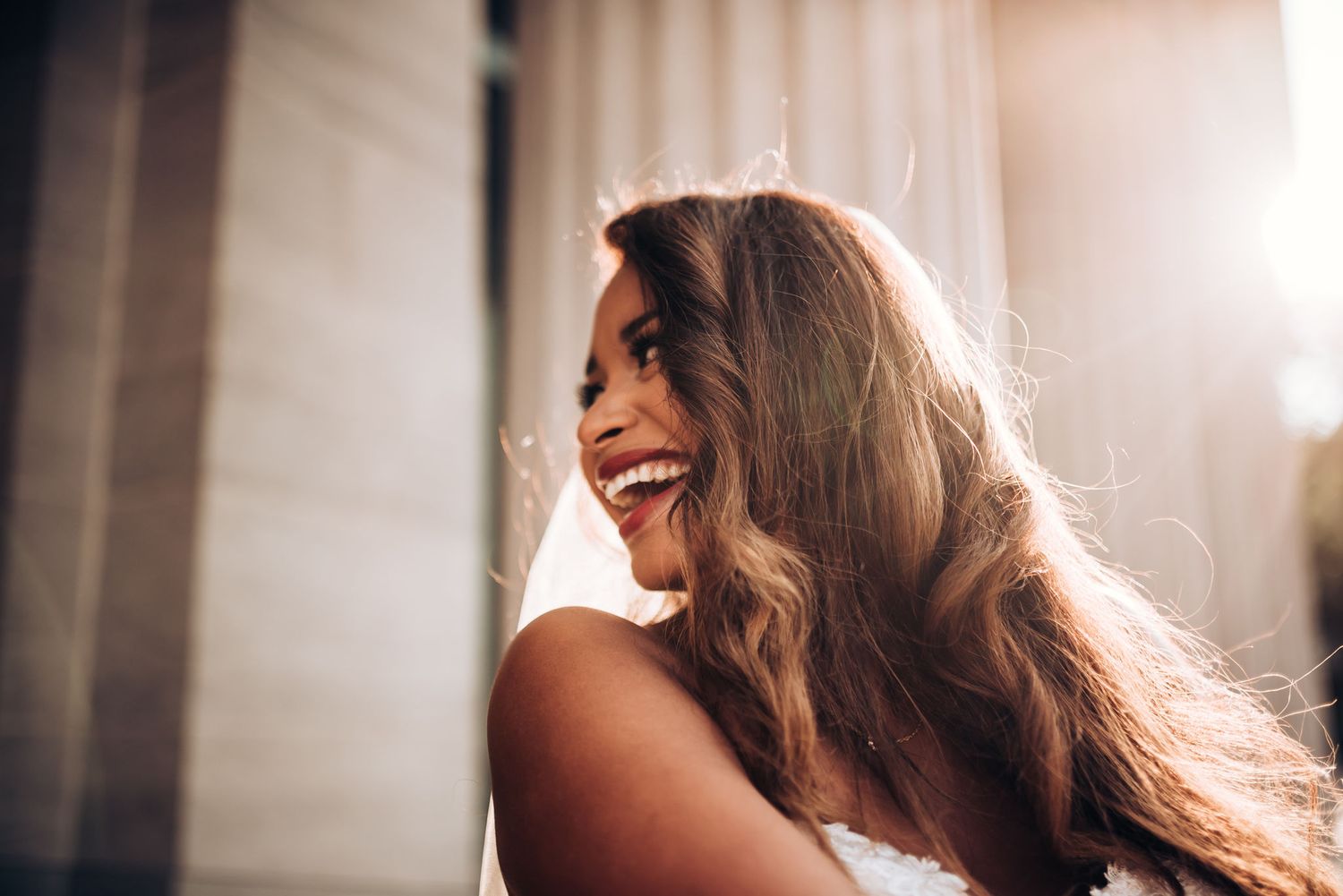 Bride with flowing hair laughs joyfully in sunlit wedding portrait.