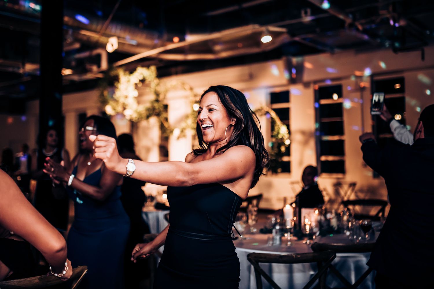 A guest dances enthusiastically at a wedding reception with round tables in the background.