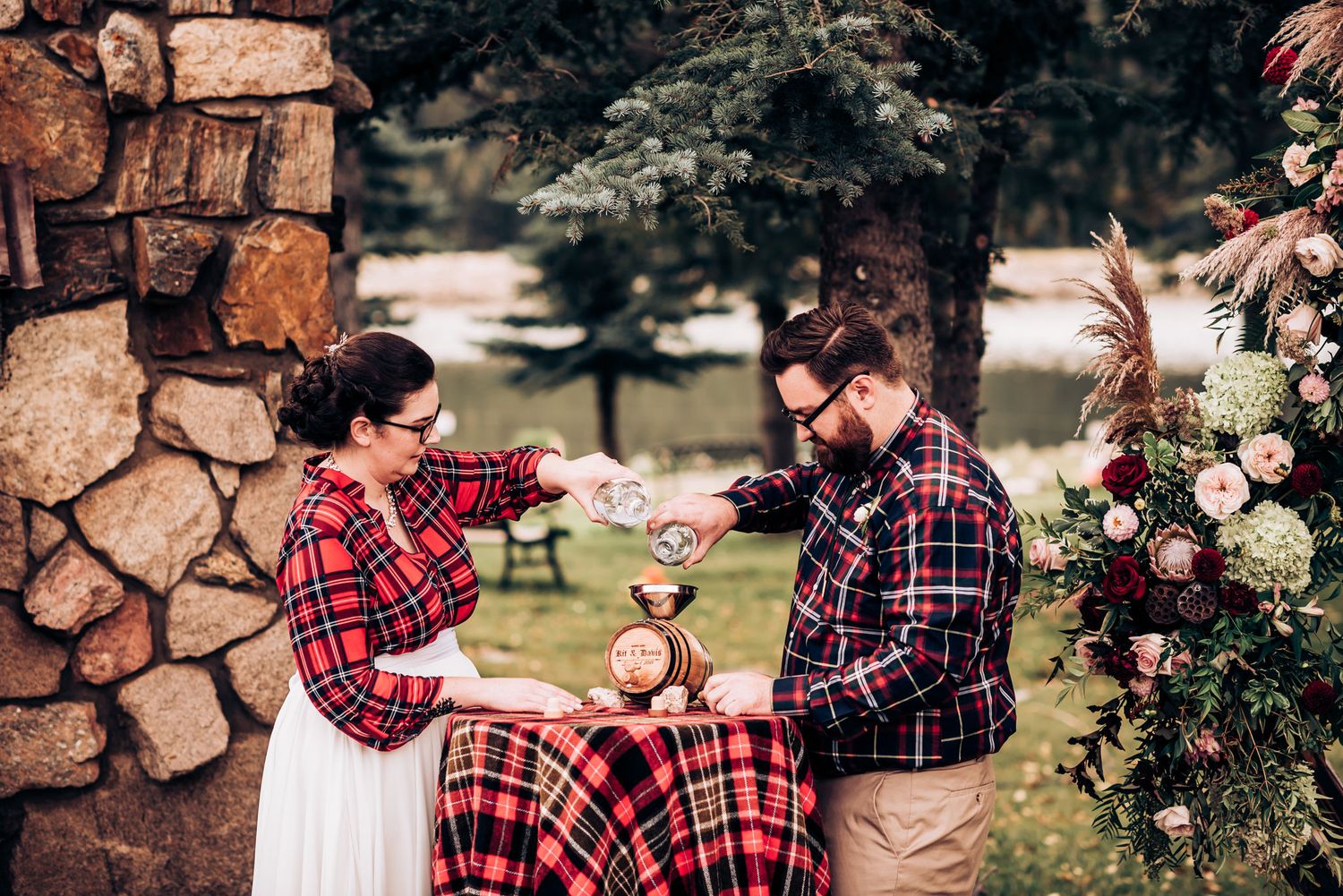 A couple in matching plaid outfits celebrates during their rustic outdoor wedding ceremony.