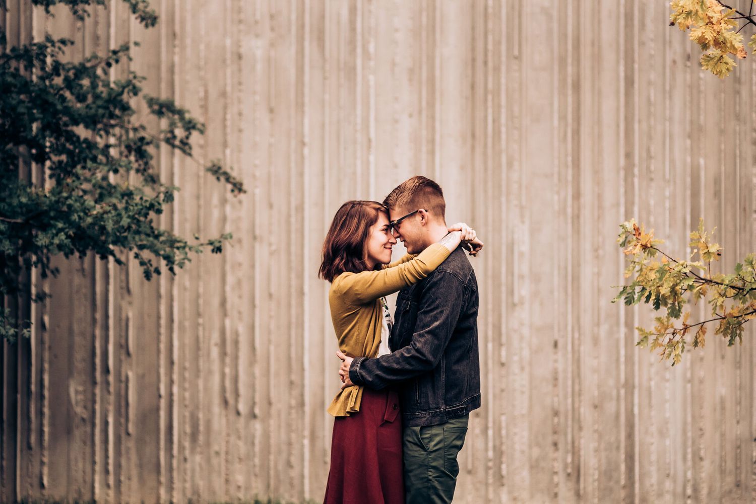 Couple in casual attire standing on grass near modern building.