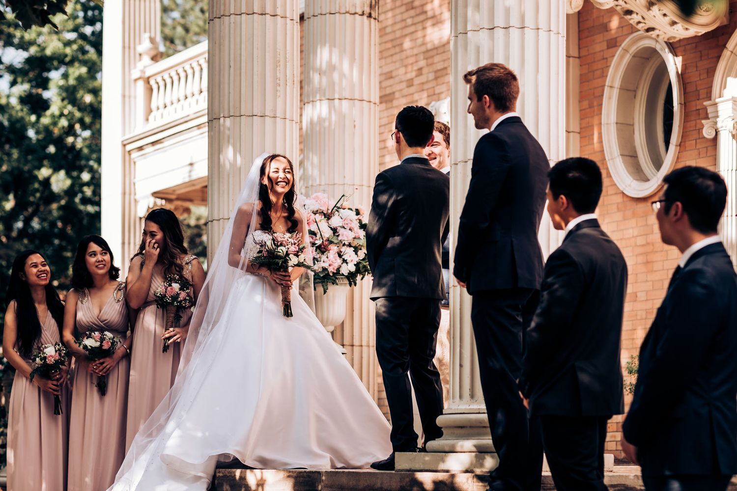 Wedding ceremony unfolds on grand stone steps with bridal party in blush gowns.