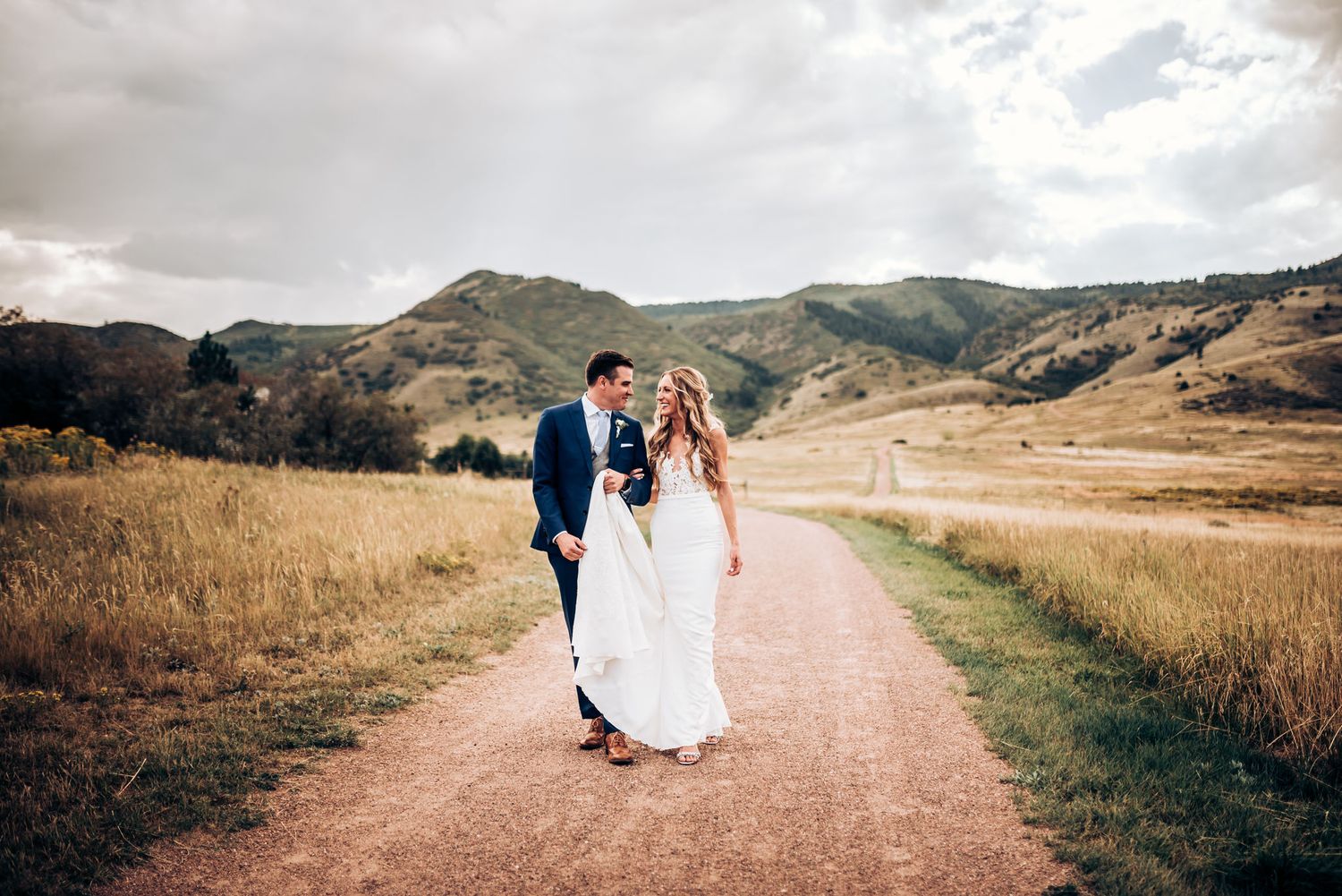 Couple walks hand in hand along mountain trail with stunning natural backdrop.